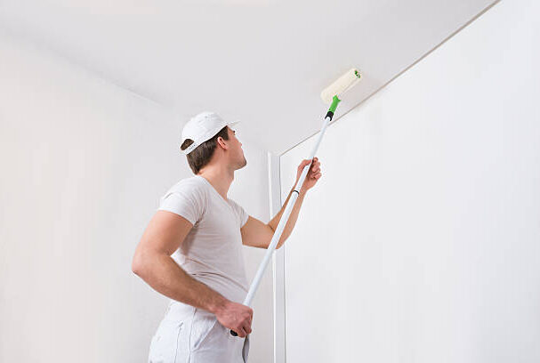 Young Painter In White Uniform Painting With Paint Roller On Wall